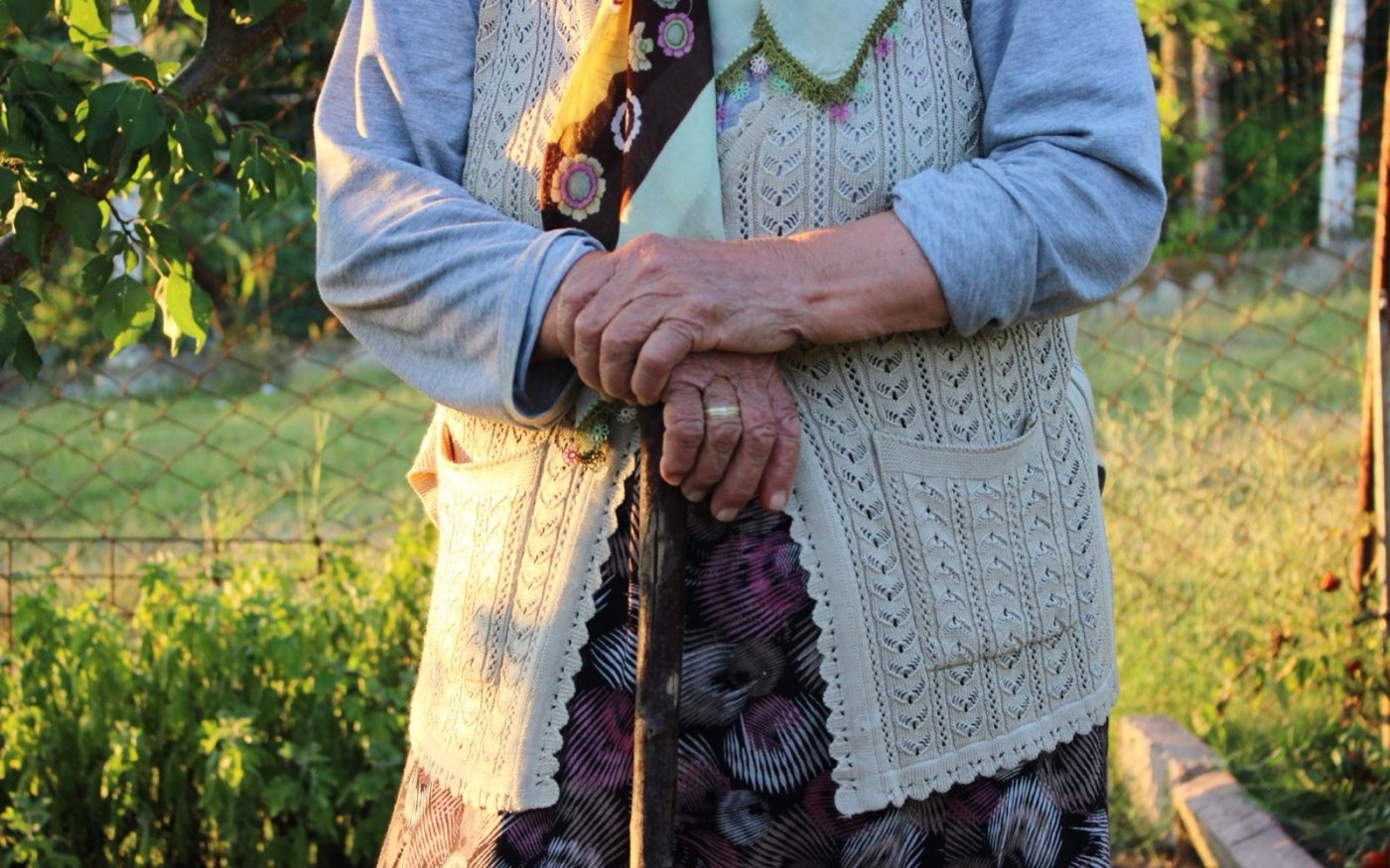 An older person's hands resting on a walking stick